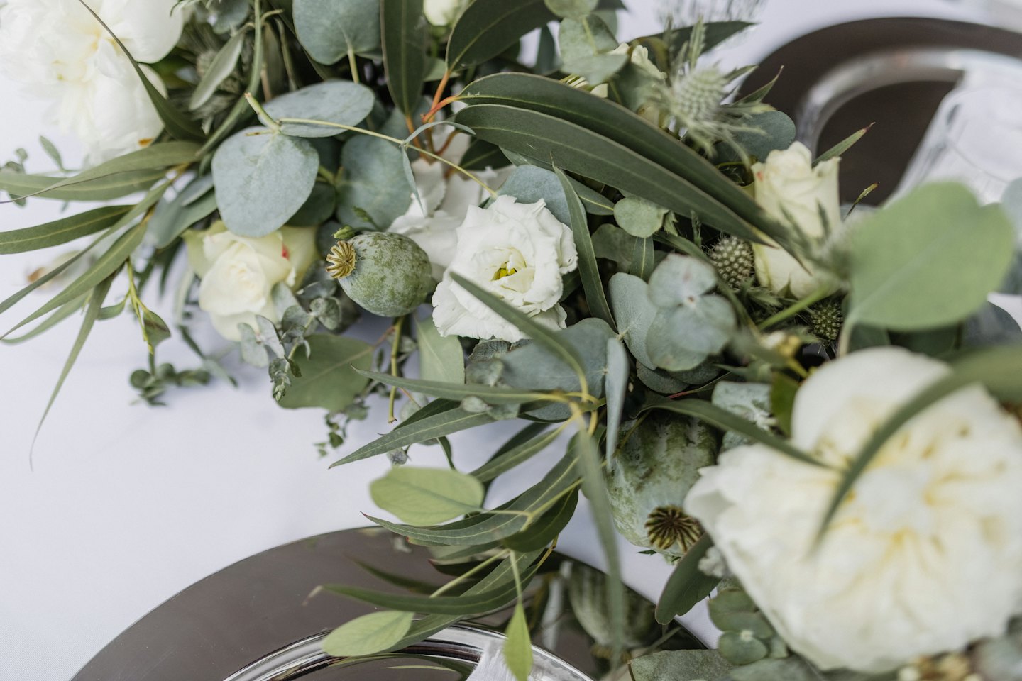 Elegant white flowers and eucalyptus leaves arranged on a silver plate.