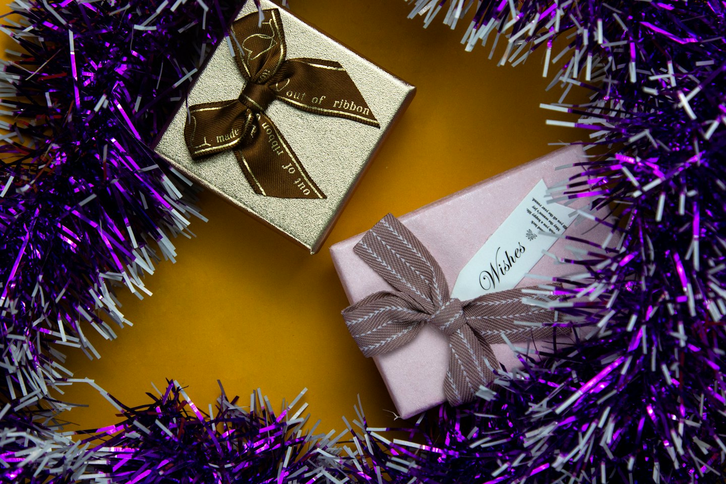 Gold and pink gift boxes on a yellow background with tinsel.